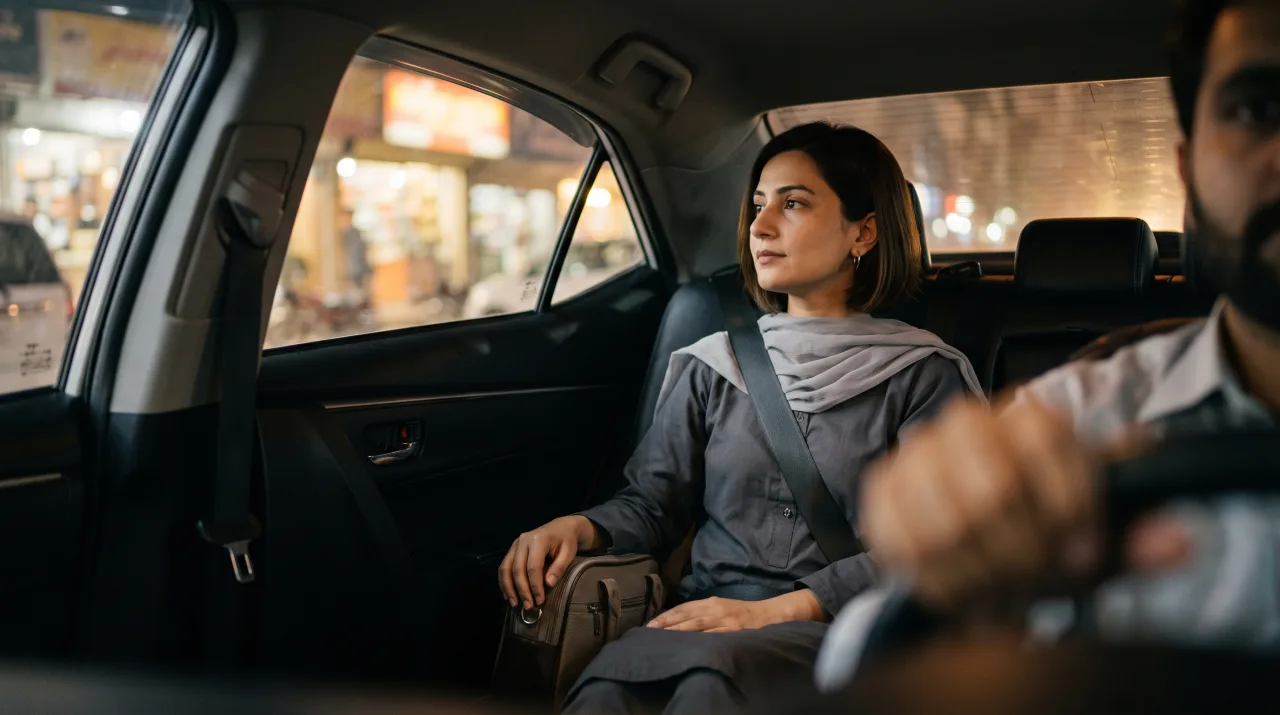 A woman in the back seat of a Sahraye ride at night, seatbelt fastened, watching the city lights